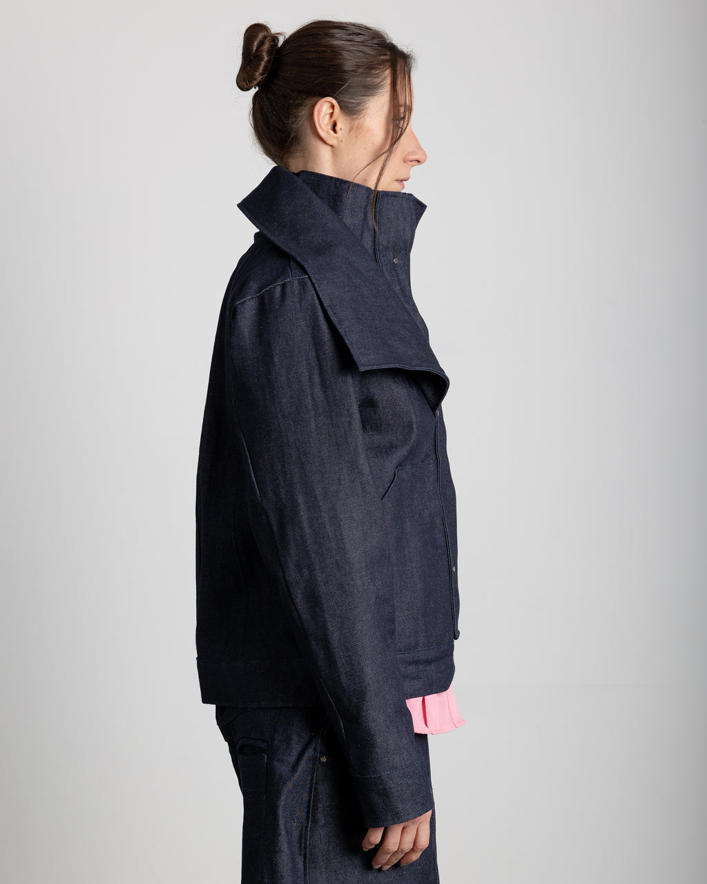 Chaqueta con cuello alto y solapas ajustables. Tapeta plisada con remaches plateados que cubren la cremallera. Bolsillos delanteros.