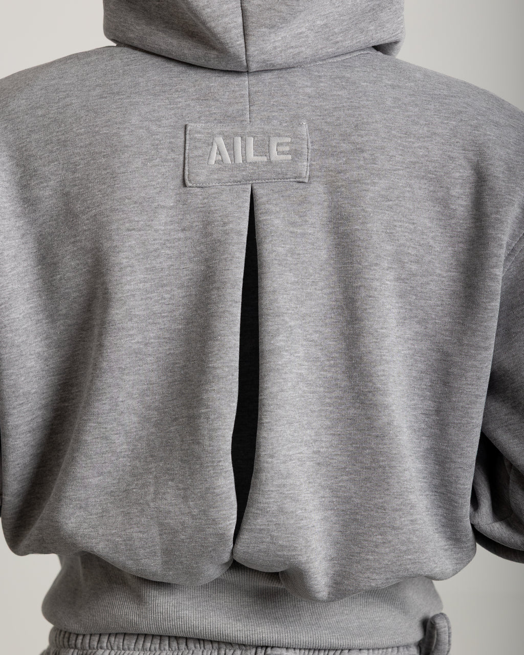Grey 100% cotton sweatshirt with a kangaroo pocket. Double hood with a drawstring on the outer hood. Pleat at the back with grey embroidery at the top. Shoulder pads on the inside to give the garment structure.